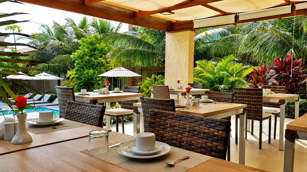 Mesas do terraço de café da manhã à sombra, com vista para o jardim tropical